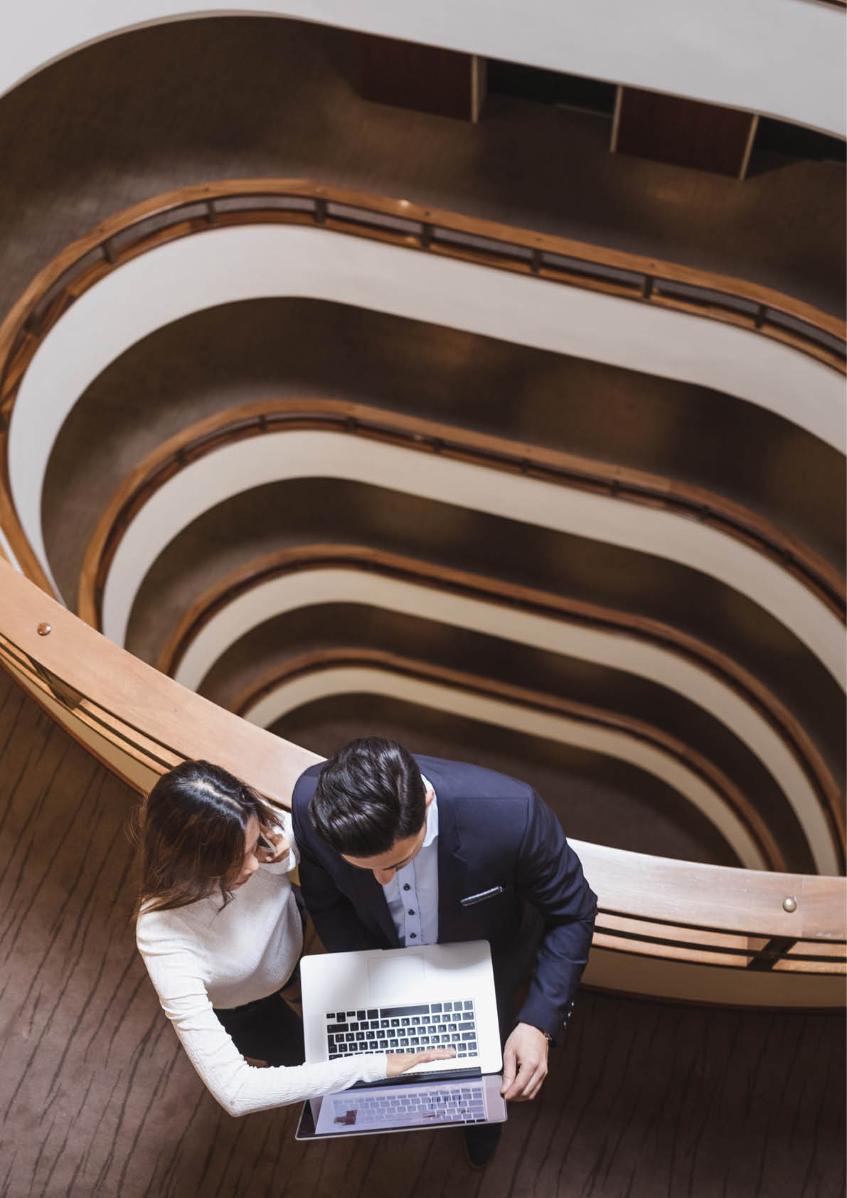 Business People Standing in the Middle of a Building's Corridor, Discussing and Using Laptop